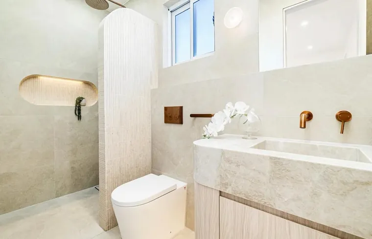 Limestone powder room with a fluted tile column, an arched backlit niche and aged brass tapware.
