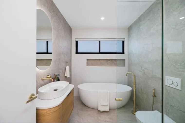 Compact ensuite with a fluted basin, arched backlit mirror and freestanding bath under a high window.