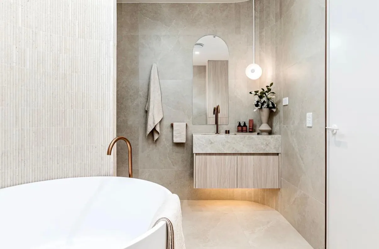 Warm neutral ensuite with a fluted tile wall, an arched mirror and a floating stone-top vanity.